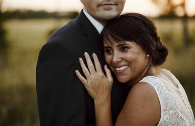 Happy beautiful bride embracing bridegroom during sunset - SAJF00055