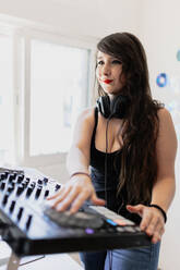 Smiling beautiful female club DJ using audio equipment at studio - MRRF00281