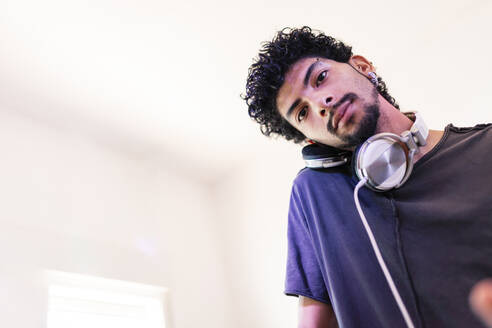 Selbstbewusster junger männlicher DJ, der im Aufnahmestudio über Kopfhörer zuhört - MRRF00291