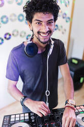 Smiling young male musician with sound mixer DJing at recording studio - MRRF00292