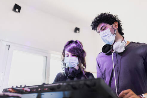 Pärchen mit Gesichtsmasken beim Abmischen von Techno-Sound im Tonstudio - MRRF00305
