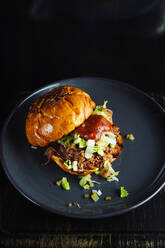 Von oben köstliche Gourmet-Hamburger mit gehackten grünen Kräutern und Tomatensauce auf schwarzem Keramikteller auf schwarzem Hintergrund serviert - ADSF12008