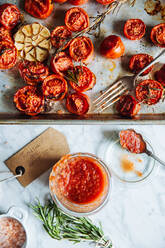 Draufsicht auf einen Glastopf mit hausgemachter Tomatensauce, der auf einem Tisch neben einem Metalltablett mit gegrillten Tomaten mit Knoblauch und Rosmarin steht - ADSF12009