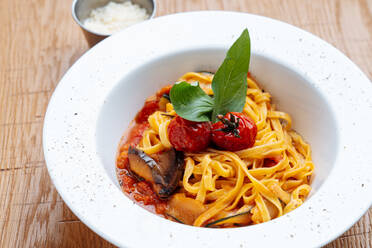 Von oben weißer Teller mit Spaghetti mit Zucchinischeiben mit gekochten Tomaten, roter Soße und Basilikumblatt - ADSF12032