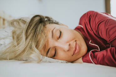 Junge hübsche Frau im Schlafanzug lächelnd beim Schlafen auf dem Bett im Schlafzimmer - ADSF12064
