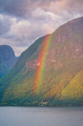 Mysterious landscape of colorful rainbow in rocky mountains in calm water under cloudy sky in Norway - ADSF12075