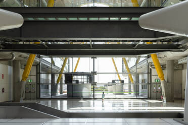 Back view of child standing in spacious terminal of international airport in futuristic style and looking out of window while waiting for departure - ADSF12099