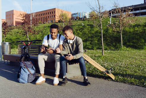 Junge schwarze Männer sitzen mit Smartphone auf einer Bank - ADSF12102