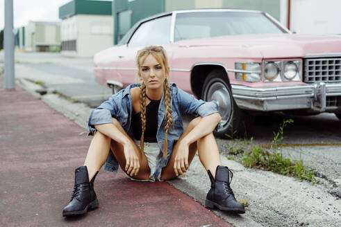 Attraktives blondes Mädchen sitzt auf dem Bürgersteig in der Nähe eines klassischen rosa Auto - ADSF12110
