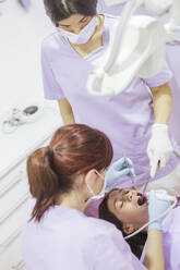 Zahnärztin in Uniform und Maske mit weiblicher Assistentin in einer modernen Zahnklinik bei der Zahnbehandlung eines Patienten - ADSF12122