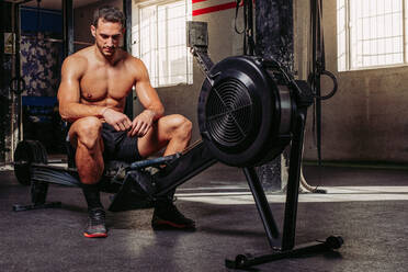 Starker Sportler, der ein Trainingsgerät im Fitnessstudio benutzt, während er während des Trainings Muskeln aufpumpt - ADSF12123
