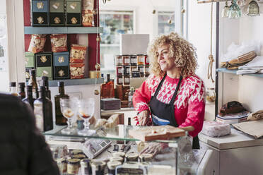 Senior man choosing food from freezer while buying wine and cheese from female seller in cozy small store - ADSF12128