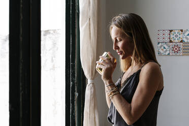 Woman holding cup while standing by window - RDGF00083