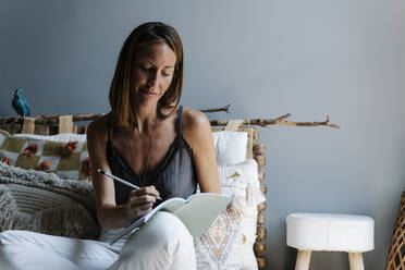 Beautiful woman writing in diary while sitting against wall - RDGF00091