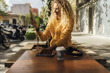 Lächelnde junge Studentin, die in einem Straßencafé in der Stadt sitzt und fotografiert - BOYF01347