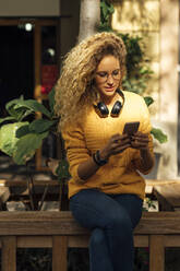 Beautiful young female student with long curly blond hair using smart phone in city - BOYF01351