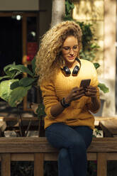 Schöne junge Studentin mit langen lockigen blonden Haaren, die ein Smartphone in der Stadt benutzt - BOYF01351