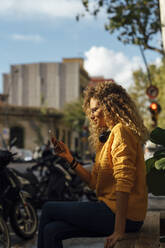 Young woman using smart phone while sitting on bench in city - BOYF01355