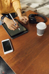 Midsection of young female student using digital tablet at sidewalk cafe table - BOYF01373