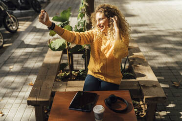 Smiling young female student taking selfie while sitting at sidewalk cafe in city - BOYF01375