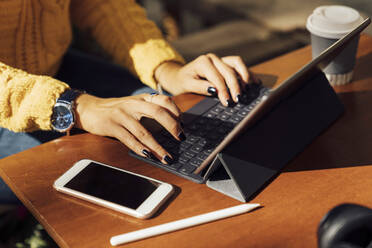 Mittelteil einer jungen Studentin, die ein digitales Tablet in einem Straßencafé in der Stadt benutzt - BOYF01384