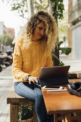 Schöne blonde Studentin, die ein digitales Tablet benutzt, während sie in einem Straßencafé in der Stadt sitzt - BOYF01385
