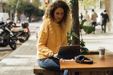 Young female student using digital tablet while sitting at sidewalk cafe in city - BOYF01386