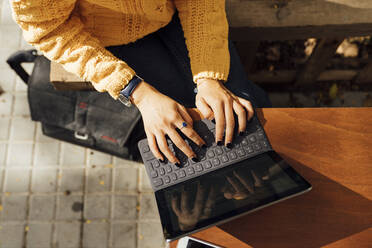 Mittelteil einer Studentin, die auf einer digitalen Tablet-Tastatur tippt, während sie in einem Straßencafé in der Stadt sitzt - BOYF01388