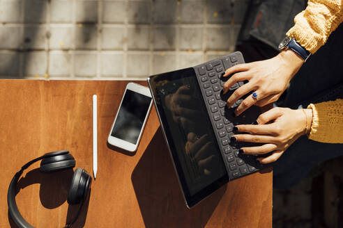 Hände einer Studentin, die auf einer digitalen Tablet-Tastatur tippt, während sie in einem Straßencafé in der Stadt sitzt - BOYF01389