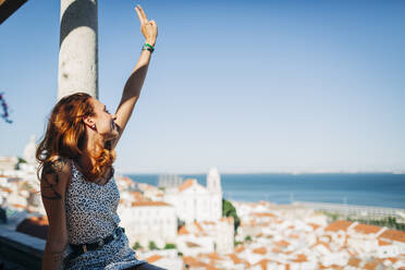 Junge Frau, die in der Alfama, Lissabon, Portugal, sitzt und ein Friedenszeichen macht - DCRF00653