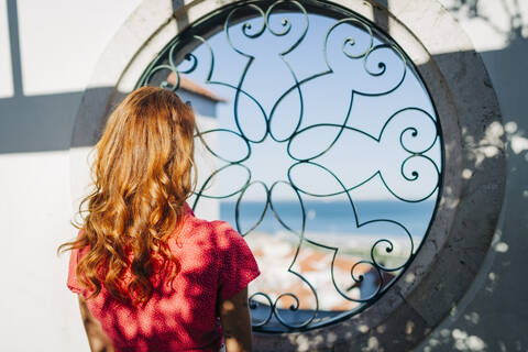 Young woman admiring view through circular window at Alfama, Lisbon, Portugal stock photo