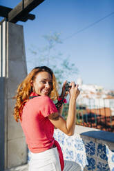 Young woman using camera while standing by retaining wall at Alfama, Lisbon, Portugal - DCRF00661