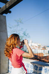 Frau fotografiert die Aussicht, während sie an einer Stützmauer in Alfama, Lissabon, Portugal, steht - DCRF00663