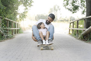 Lächelnder Vater und Tochter beim Skateboardfahren auf dem Fußweg im Park - JCZF00182