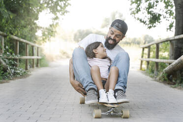 Fröhlicher Vater und Tochter beim Skateboardfahren auf dem Fußweg im Park - JCZF00183