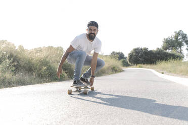 Gutaussehender Mann fährt Skateboard auf der Straße gegen den klaren Himmel - JCZF00184