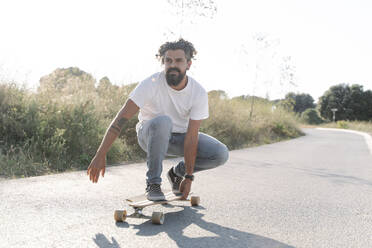 Hübscher bärtiger reifer Mann fährt auf der Straße Skateboard gegen den klaren Himmel - JCZF00185