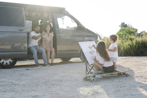 Happy parents sitting in van while daughter painting by sister during sunset stock photo