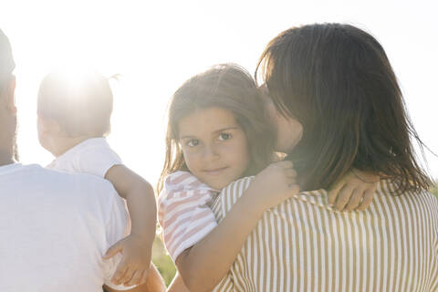 Cute girl embracing mother by father with sister at park during sunset stock photo
