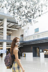 Redhead woman walking indoors while wearing protective face mask - MTBF00597