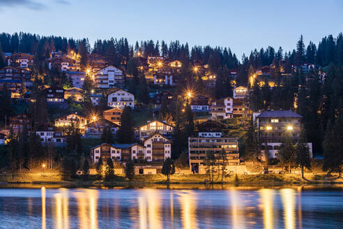 Schweiz, Kanton Graubünden, Arosa, Beleuchtete Chalets am Ufer des Obersees in der Sommerdämmerung - WDF06173