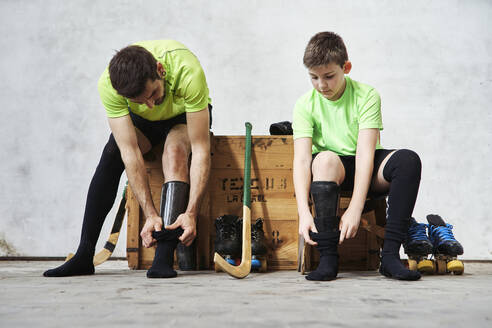 Father and son wearing socks while sitting on wooden box at court - VEGF02809