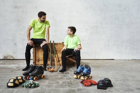 Vater und Sohn unterhalten sich, während sie auf einer Holzkiste neben einem Sportgerät an der Wand im Gericht sitzen - VEGF02811