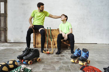 Father sharing light moment with while sitting on wooden box by sports equipment against wall at court - VEGF02812