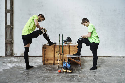 Father and son wearing kneepads by wooden box near wall at court - VEGF02816