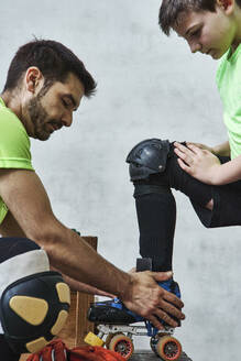 Man helping son wearing roller skate before training - VEGF02819