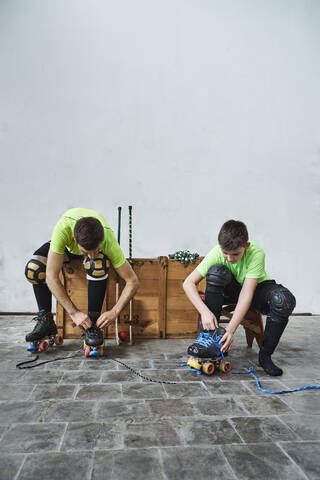 Vater und Sohn mit Rollschuhen an einer Holzkiste an der Wand im Gericht, lizenzfreies Stockfoto