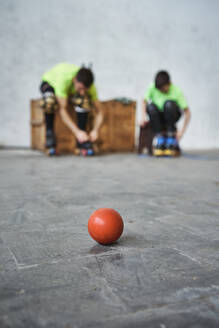 Close-up of red hockey ball on floor against father and son wearing roller skates at court - VEGF02823