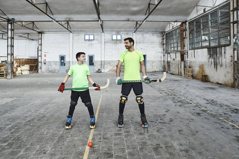 Mature man and his son holding hockey sticks while looking at each other - VEGF02829