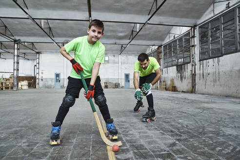Mature man with son practicing roller hockey on court - VEGF02843